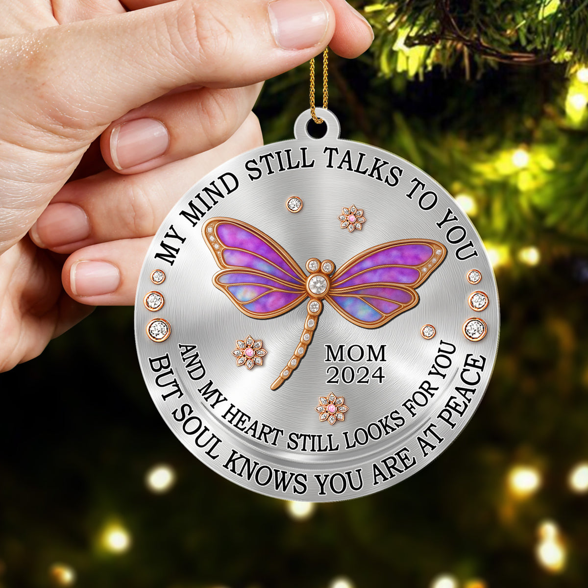 Decorative ornament with butterfly design and engraved text, held against a Christmas tree background.